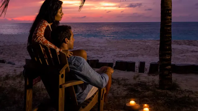 A couple watching the sunset from the beach with candles lit in the sand