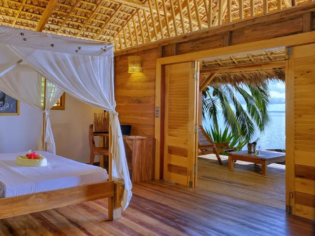 Beach bungalow bedroom with a mosquito-netted bed and doors folded open to a deck above the sea