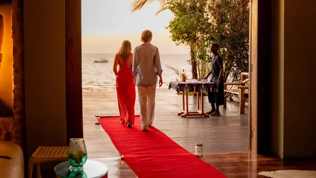 A couple walking out along a red carpet to sundowners on a beachfront deck
